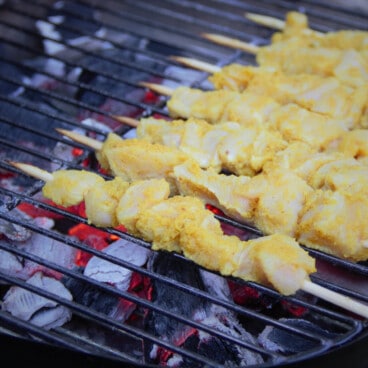 Raw chicken satay on a small grill with red charcoal underneath.