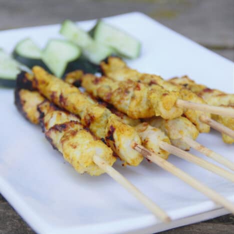 Looking across a rectangular plate with a pile of chicken satay and a side of cucumber chunks.