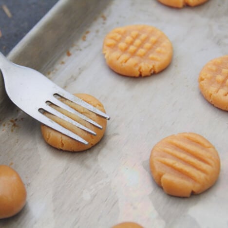 Cookie dough on a baking tray with a fork being used on one of them the create the hatch top.