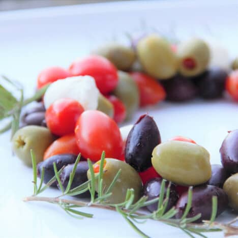 Looking into a white plate with the antipasto Christmas wreath, with olives, tomatoes, and rosemary.