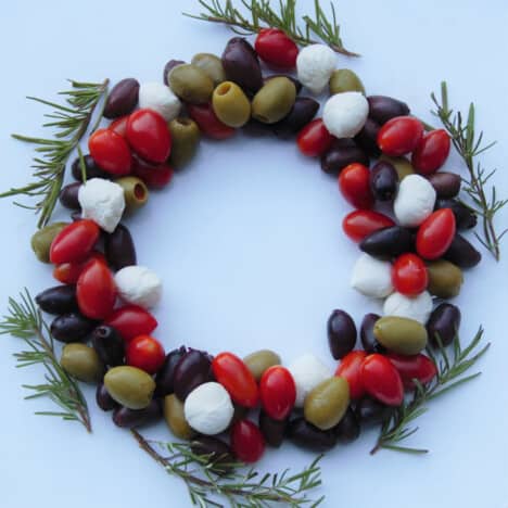 Looking down on a beautiful arrangement of olives, tomatoes, mozzarella cheese, and rosemary sprigs on a white platter.