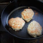 Three Asian-inspired turkey rissoles cooking in a skillet, the tops are golden brown.