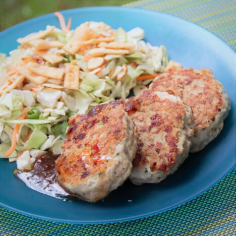 Three Asian-inspired turkey rissoles are served on a blue camp plate with a side of Asian-inspired salad.
