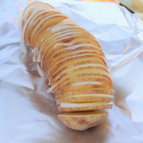 A raw Hassleback potato is sitting on a sheet of foil with each sliced filled with onion.