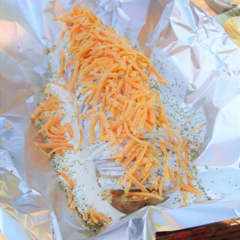 A prepared raw baked potato with cream and cheese, ready to wrap in the foil it is sitting on.