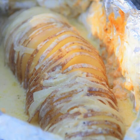 Looking longways down a creamy baked potato still sitting in the foil it was cooked in.