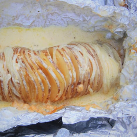 A baked potato sitting in a pool of creamy cheese sauce, in foil.
