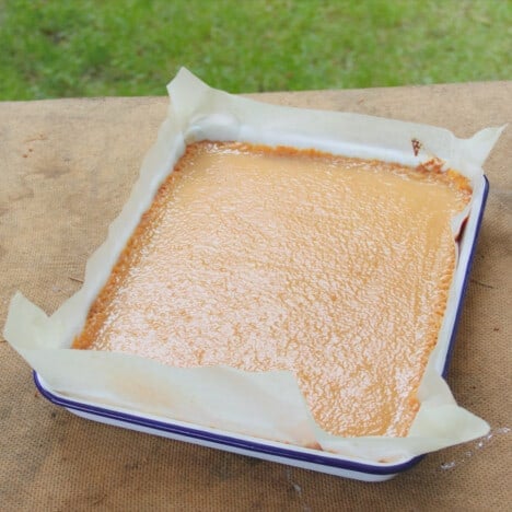 A parchment paper-lined tray with the baked cookie base and caramel sauce within.