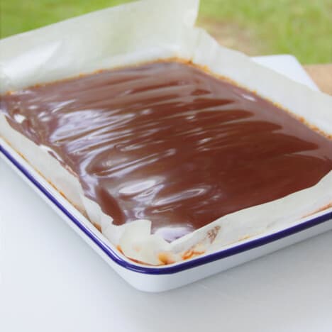 The completed tray of caramel slice sitting on a table with the chocolate top layer showing.