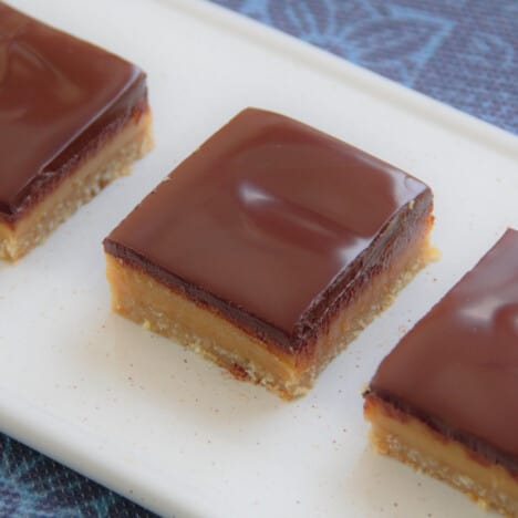 Caramel slice squares laid out on a white serving tray.