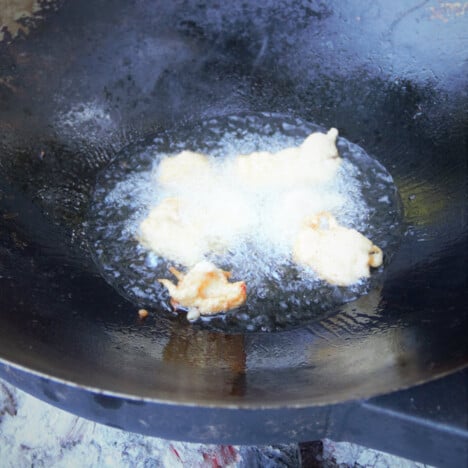 Battered pieces of chicken frying in the wok over hot coals.