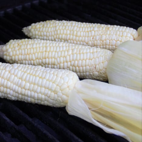 Three cobs of corn cooking on a grill.