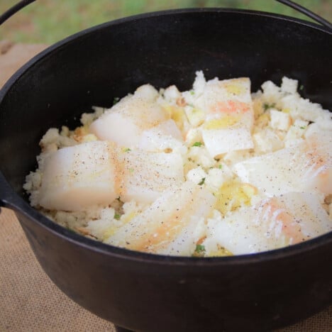 A Dutch oven with a layer of seasoned bread topped with fillets of white fish.