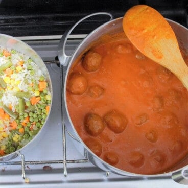 Looking down on a gas stove with a pot of meatball tikka masala and a pot of pilau rice.