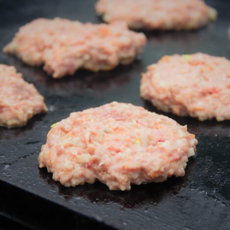 Five round nangari burger patties are on the grill but have not had their first flip.