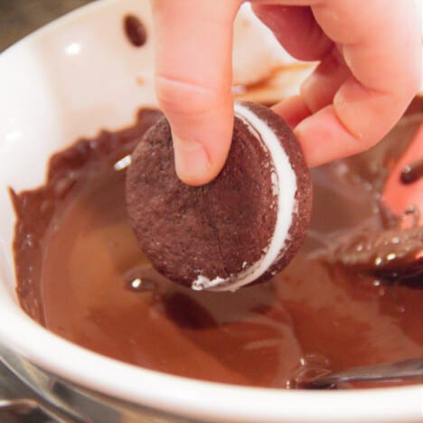 A bowl of melted chocolate with a peppermint cream sandwich being placed into it to be coated with chocolate.