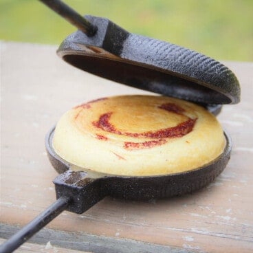 A pie iron cracked open showing a cooked cinnamon roll.