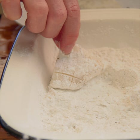 One piece of squid being dusted with the cornstarch, salt, and pepper mixture.