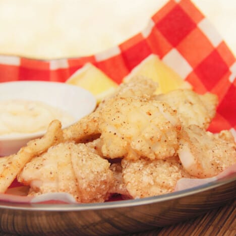 A serving of salt and pepper squid served on a red check napkin with tartar sauce.