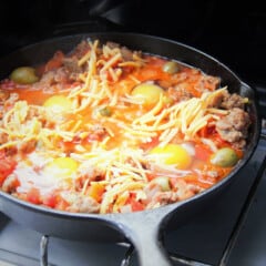 A cast iron skillet with the eggs cracked into the tomato and pork sausage sauce, ready for the final stage of cooking.