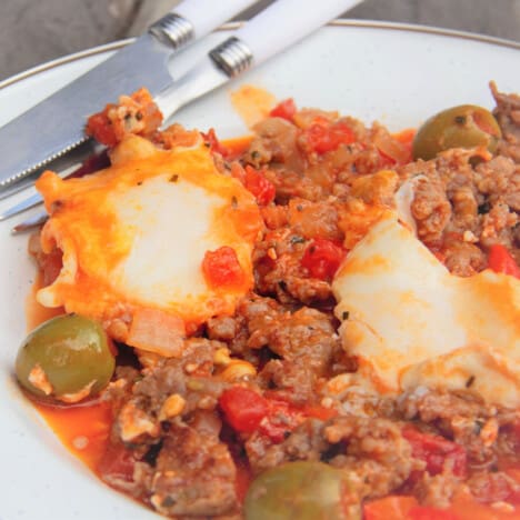 Close up of the Shakshuka showing two firm cooked eggs, sausage, and green olives.