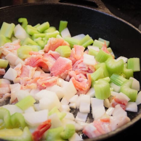 Raw diced bacon, onion, and celery in a skillet ready to sauté.