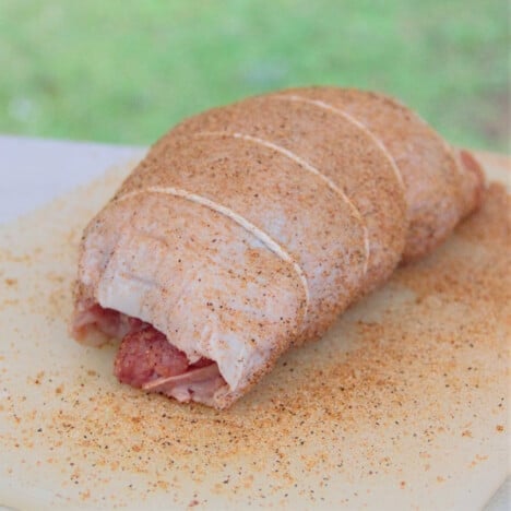 The raw smoked turkey roll is prepared and tied with the butcher's twine, sitting on a chopping board.