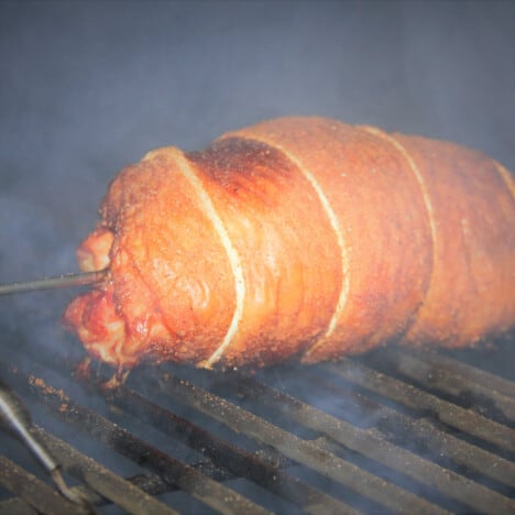 A golden brown turkey roll sits on grates in a smoker.