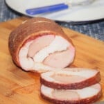 The smoked turkey roll on a chopping board with two slices showing the cross-section of the light and dark meat.