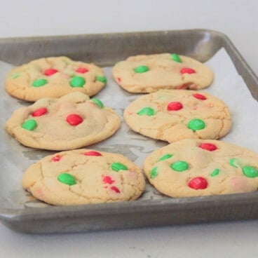 Six baked Christmas cookies with red and green candy-coated chocolates on a small baking tray.