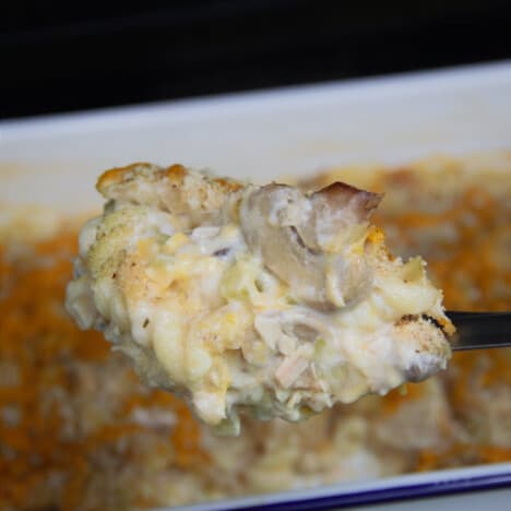 A portion of the baked tuna noodle casserole is being scooped out of a white casserole dish.