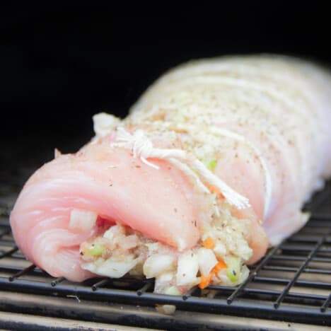 A raw stuffed turkey breast is sitting in the smoker on a rack ready to cook.