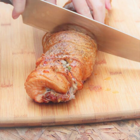 The stuffed turkey breast is being sliced on a chopping board in preparation to serve.