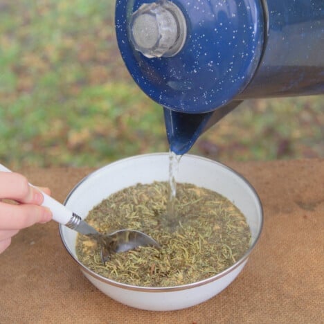 Water is poured from a blue camp kettle into a white camp bowl with the solid brine ingredients.