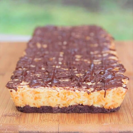 A whole finished apricot bite slice on a wooden cutting board, with clear layers of cookies, apricot center, and chocolate drizzle.