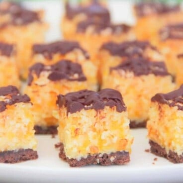 Looking into a row of cut apricot bites on a white plate, with a chocolate cookie base, apricot filling, and chocolate drizzle.