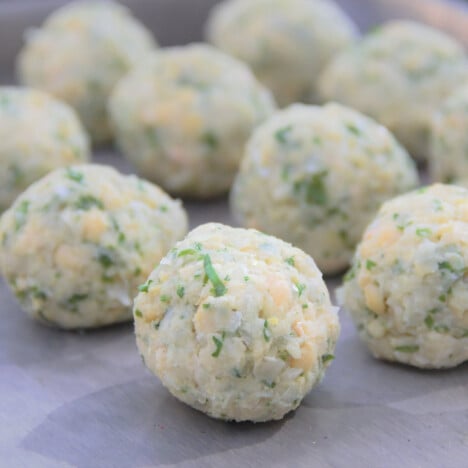 Raw balls of falafel are sitting on a silver tray ready to be cooked.