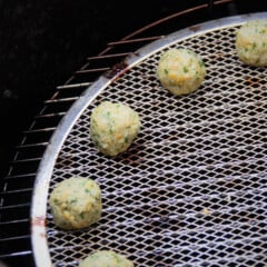 Raw falafel are shown sitting towards the edge of a stainless steel round grill grate.
