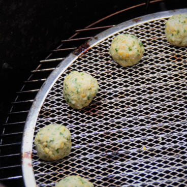 Raw falafel are shown sitting towards the edge of a stainless steel round grill grate.