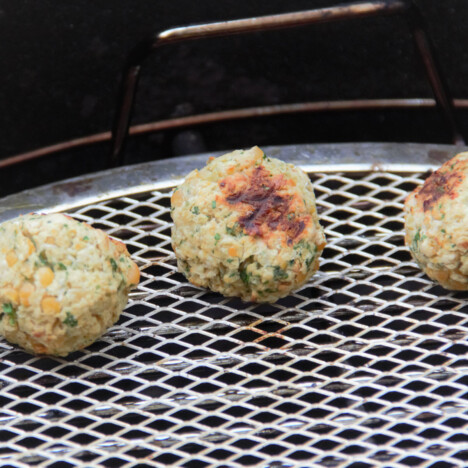 A close up view of three cooked falafel sitting on a stainless steel grilling rack.