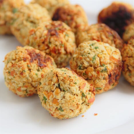 Looking down onto a white plate filled with round, golden-brown falafel balls.