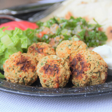 Cooked falafel are served on a camp plate with sides including tabbouleh, tomato, and lettuce.