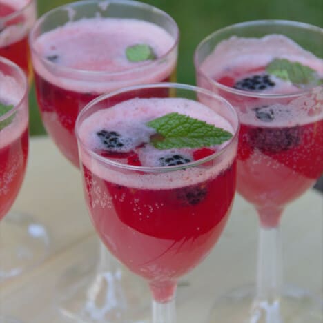 Looking down into a row of wineglasses filled with the blackberry summer mocktail and garnished with fresh mint and blackberries.