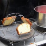 A camp gas stove with the closest burner toasting the cake and the back burner with a saucepan with the berries on it.