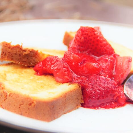 Looking across a white plate with two slices of toasted cake, topped with juicy strawberries.