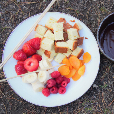 A white plate with bite-sized pieces of cake and banana, along with dried apricots, raspberries, and strawberries.