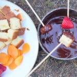 Strawberry, cake, and banana being dripped with wooden skewers into the chocolate fondue.