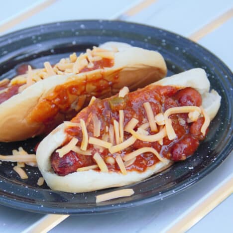 A black camp plate with two hot dogs covered in chili and toped with grated cheese.
