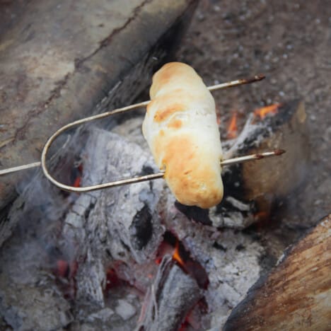 A Campfire hot dog being cooked over campfire coals on a marshmallow stick