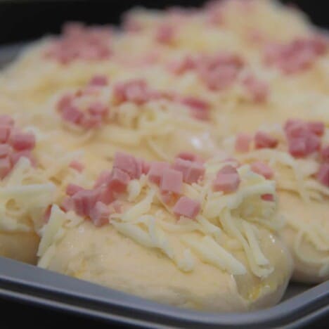 Close up on a raw cheese and bacon roll on the baking tray ready to be placed in the oven.